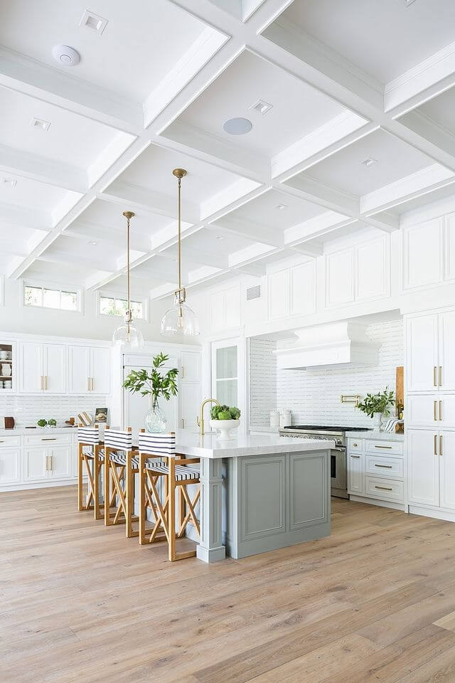 Light blue kitchen island campaign style striped island seating, white shaker cabinetry with brass hardware. Open kitchen with vaulted ceilings, glass island pendants. Bright and airy home.