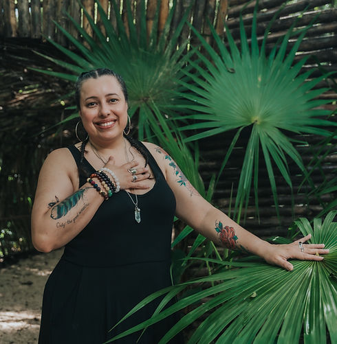 Portrait of Rebecca Rosalez standing in front of a tall palm plant, gently resting one hand on the plant and the other hand o