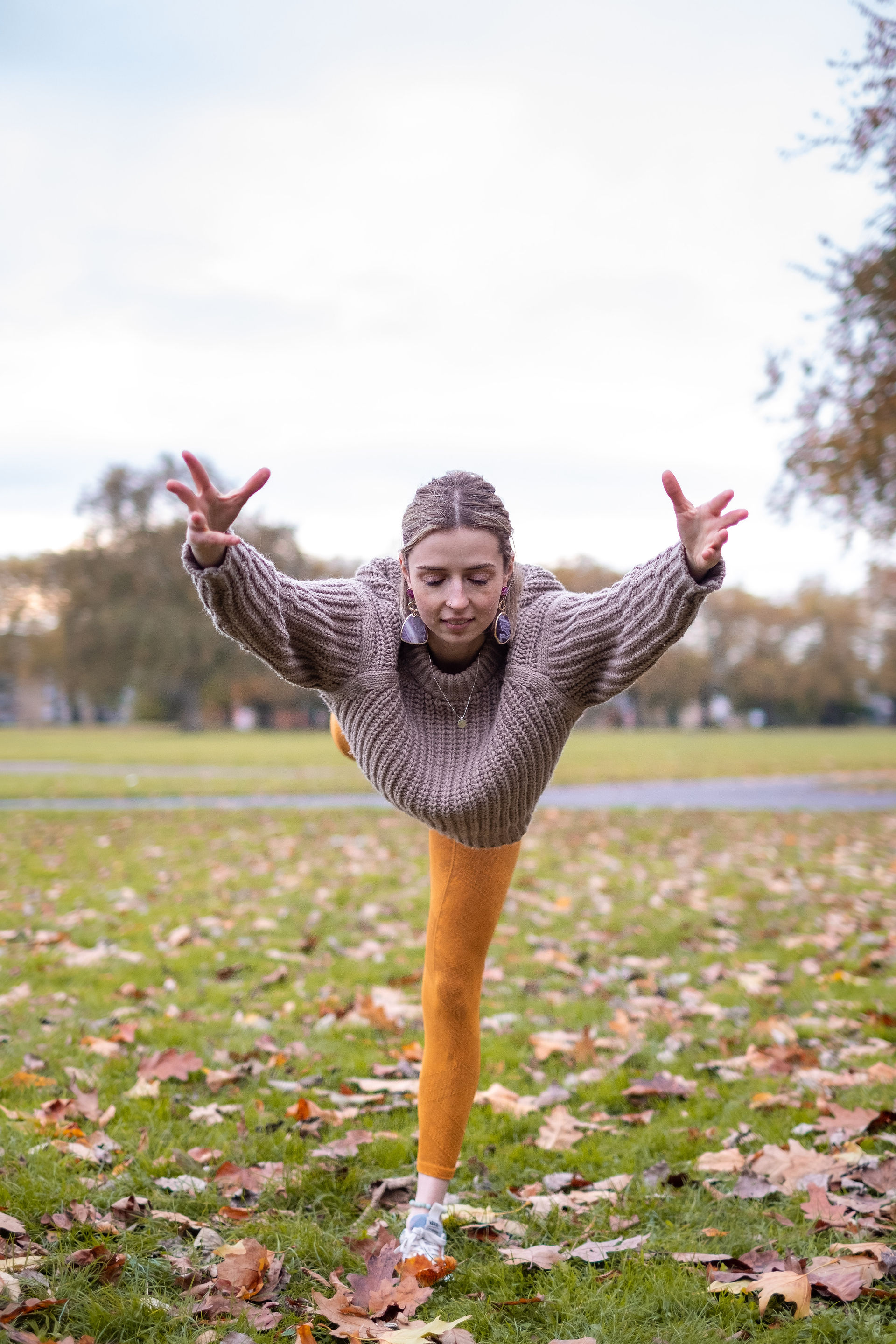 A woman in a beige jumper doing yoga in a park 