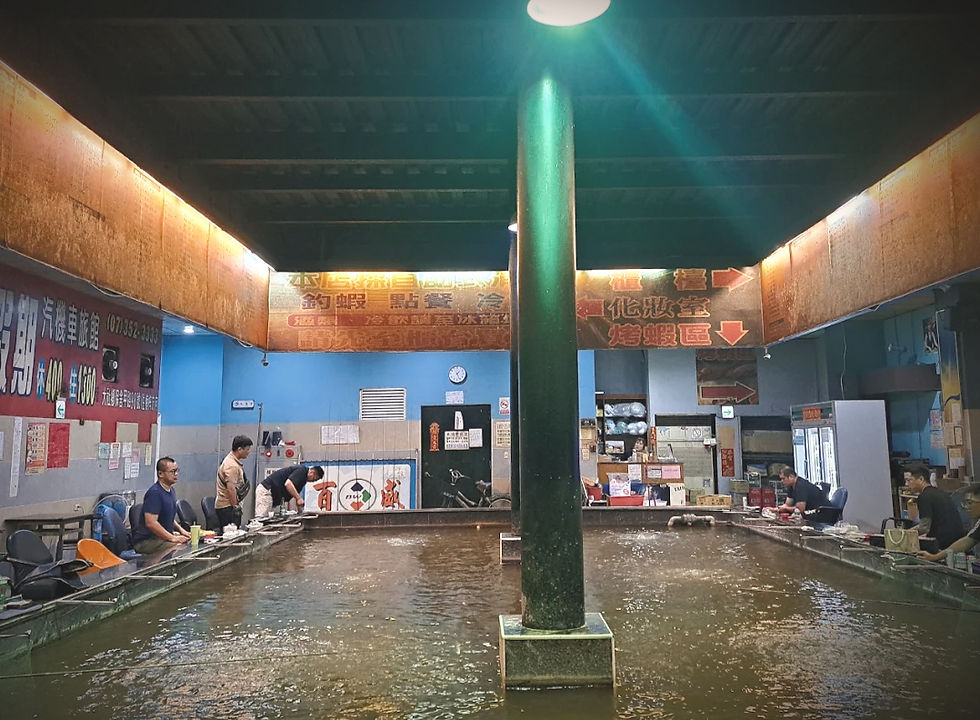 People dine around a large indoor fish tank in a Chinese restaurant, with bright signs and a central pillar under dim lights.
