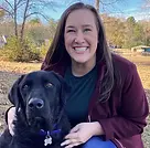 Jessie Willis, speech-language pathologist and owner of Rogers Bridge Pediatric Therapy, smiling with her black Labrador Retriever