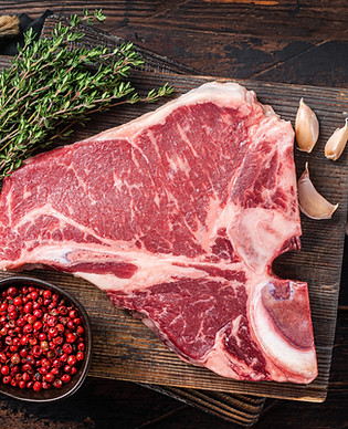 Prime T-bone beef meat steak, raw porterhouse steak on butcher board with herbs. Wooden ba