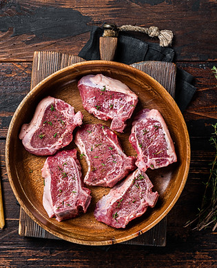 Raw lamb loin rib chops steaks in wooden plate with herbs. Wooden background. Top view.jpg