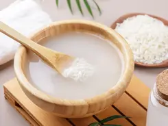 Rice water in a glass bowl surrounded by uncooked rice grains the ancient Asian beauty ritual used by Yao women in China and court ladies in Japan for centuries