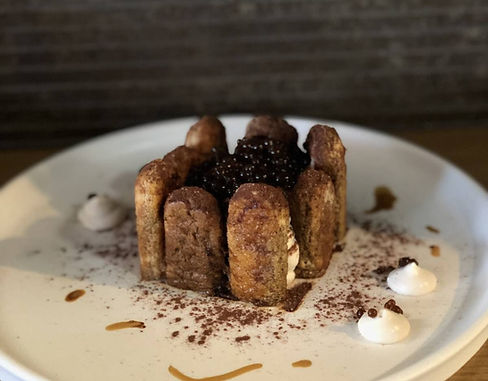 Chocolate dessert topped with pearls and cocoa powder, served on a white plate with whippe
