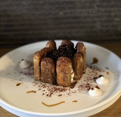 Chocolate dessert topped with pearls and cocoa powder, served on a white plate with whippe