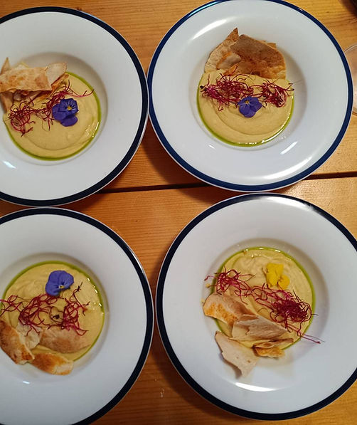 Four plates of creamy hummus with grilled pita bread and edible flowers, served on a woode