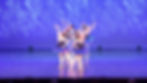 Seven young ballerinas in blue and purple tutus on stage.
