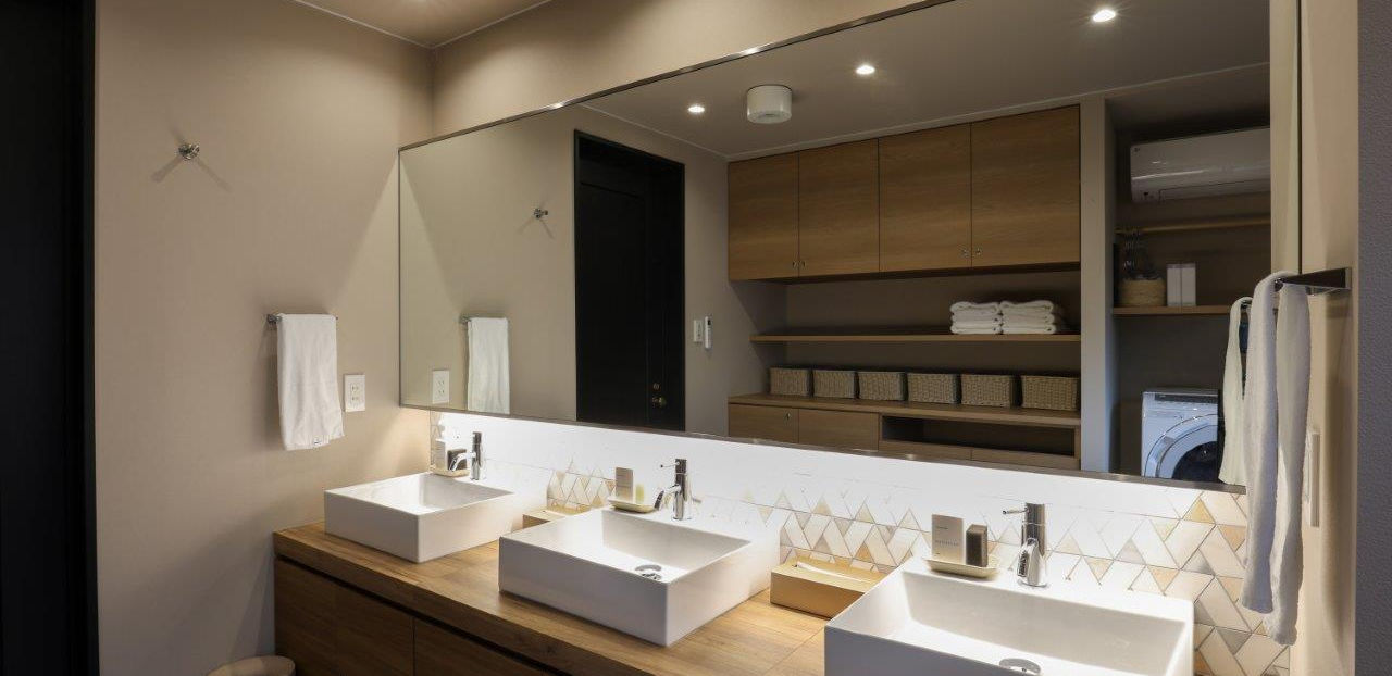 洗面ボウルが3つ横に並んでおり、その上には大きな鏡があります。お手拭き用のタオルもあります。