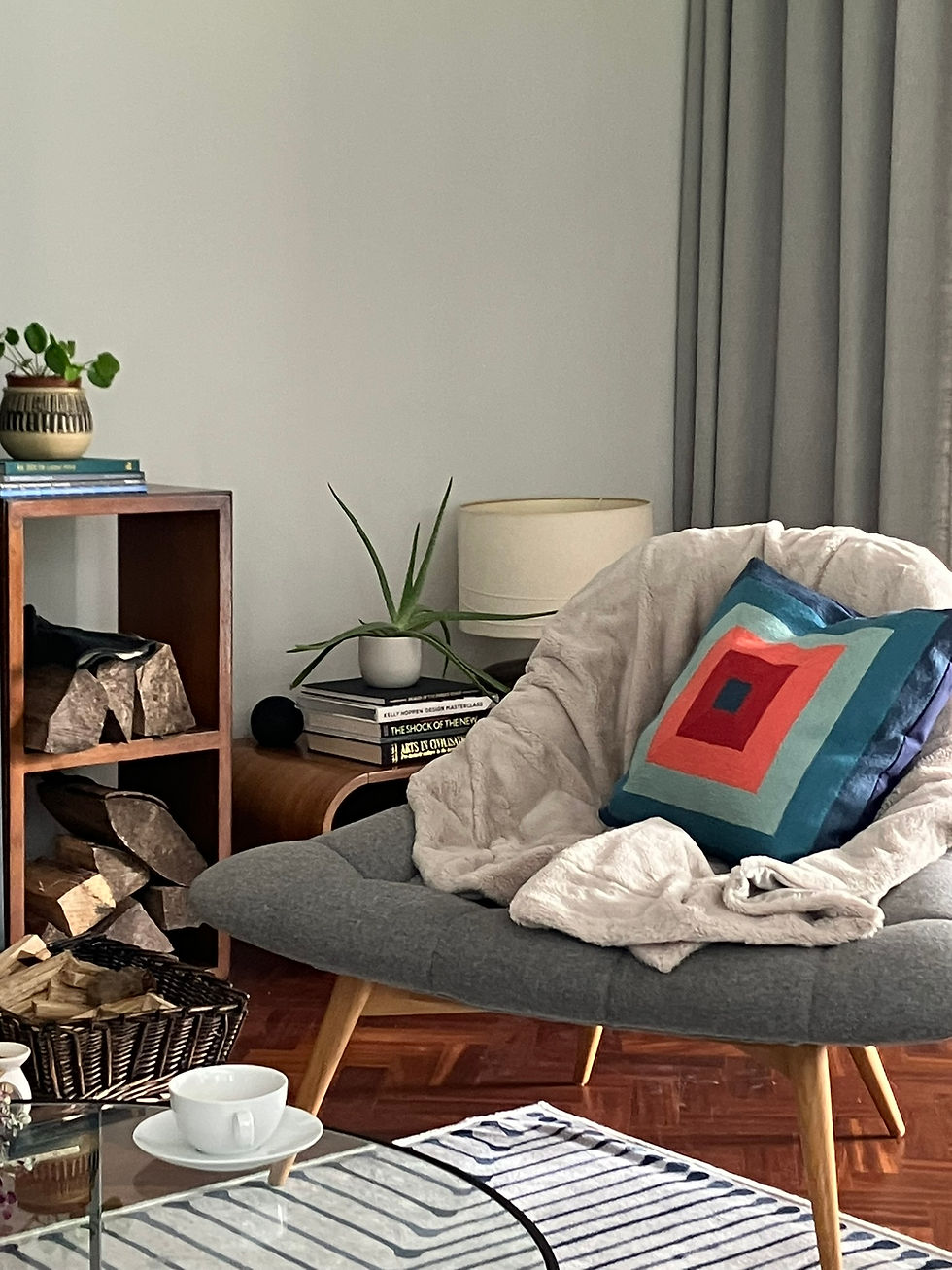 cosy chair by the fireplace with a soft grey throw and a brightly coloured john lewis cushion