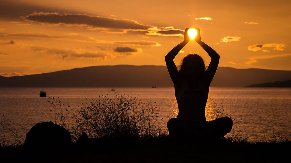 Frau sitzt in Yogapose und hält optisch die Sonne in ihren hochgestreckten Händen
