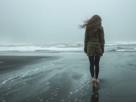 Lonely woman walking across a deserted beach facing the tide with the tide coming in.