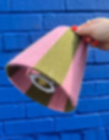 Khaki and blush rose striped yarn-wrapped lampshade held against blue brick wall