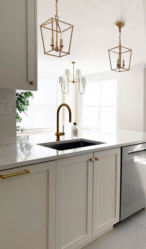 Bright white kitchen with shaker cabinets, brass hardware, quartz island countertop, and stainless steel fridge