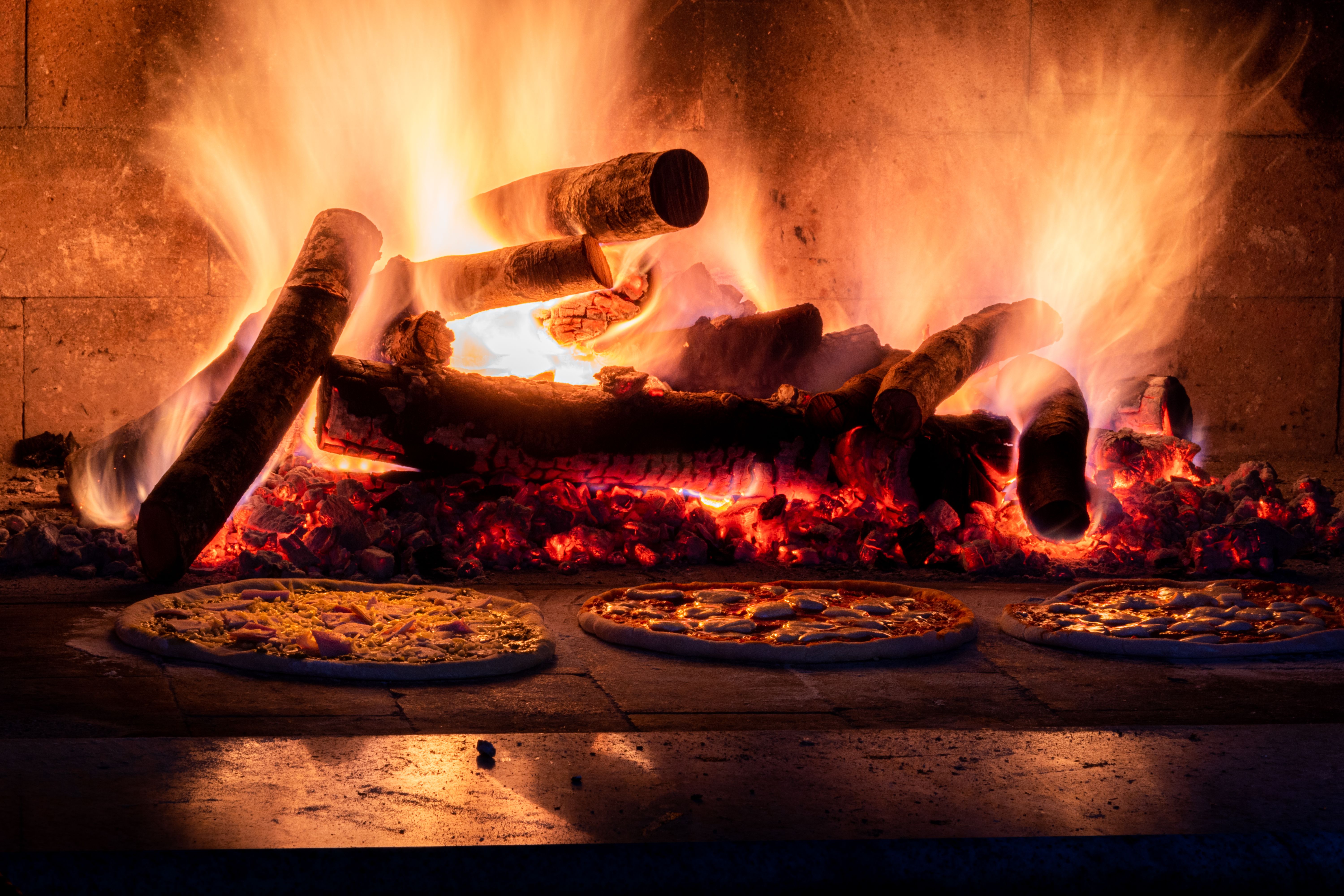 Three pizzas baking on the deck of a wood fired oven in front of the fire