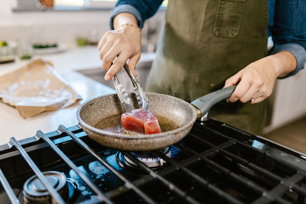 Hands lowering a tuna steak into a hot pan over a blue gas range burner