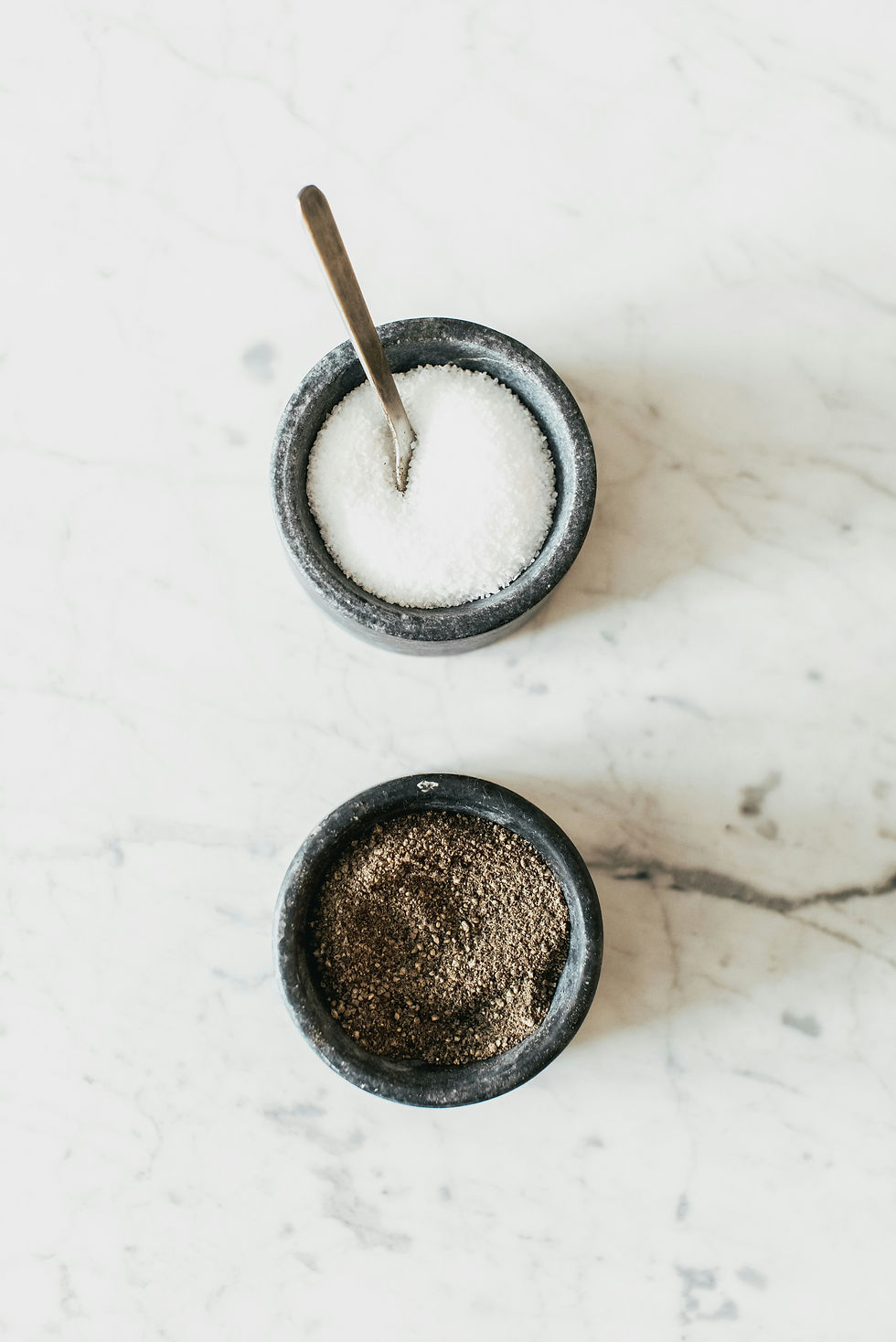 Ground black pepper and coarse salt in small bowls on a white marble surface