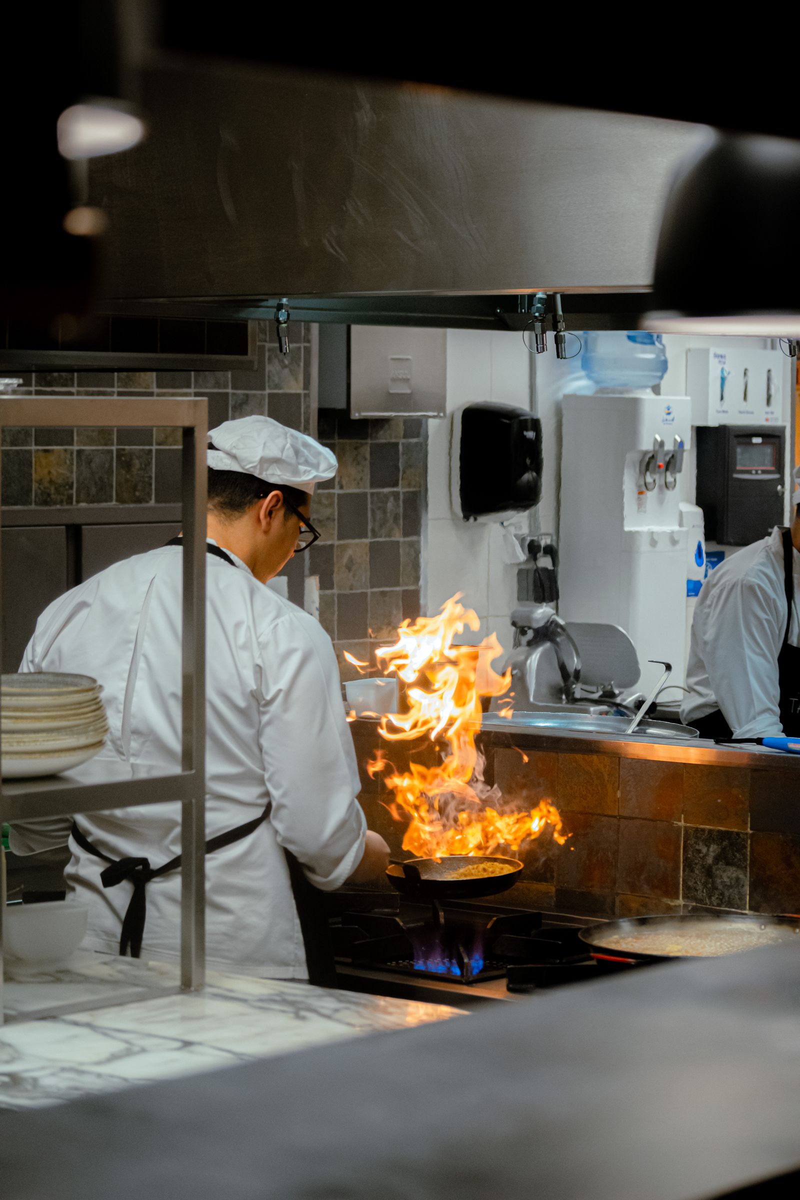 Chef flambeing a pan on a professional range, seen from behind
