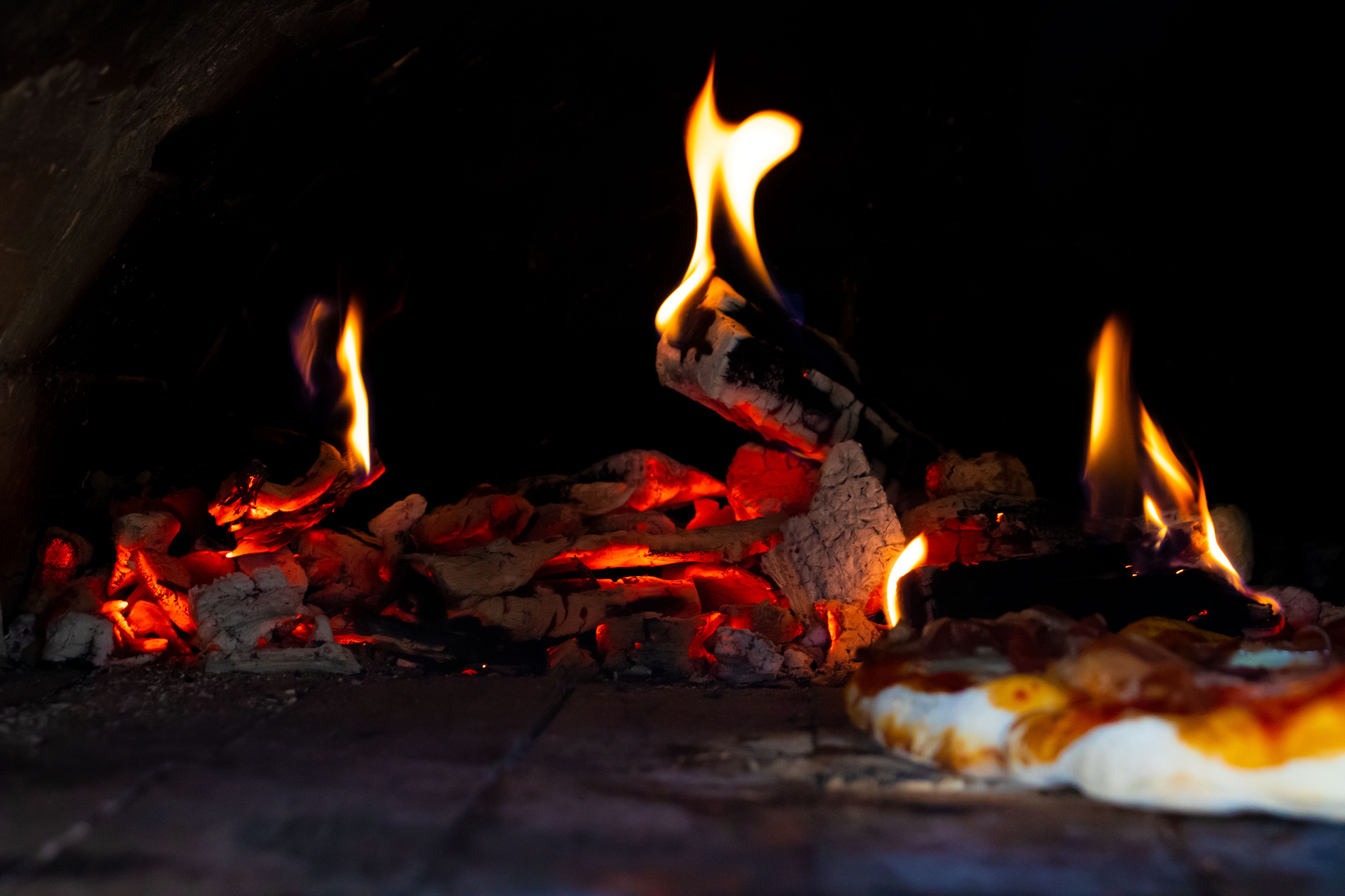 Flames and embers inside a wood fired pizza oven as a pizza bakes on the deck