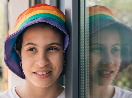 LGBTQ+ child with a rainbow bucket hat on.