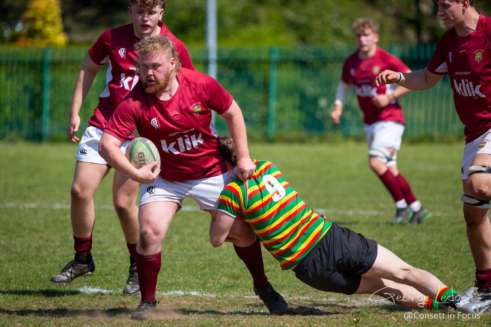 Rugby player runs with ball, tackled by opponent