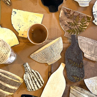 A range of printing plates in the shape of pots are layed flat on a cardboard background
