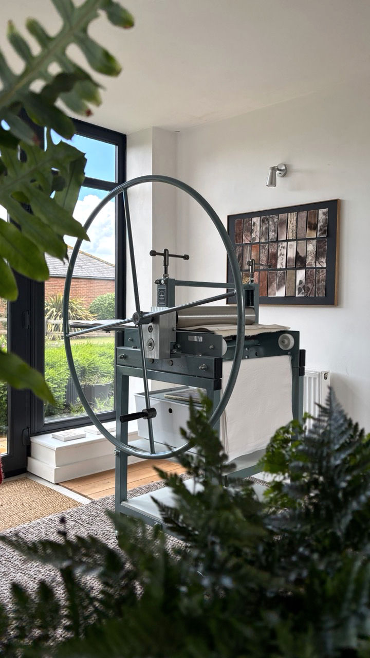 gunning etching press in studio with plants in the foreground and art on wall
