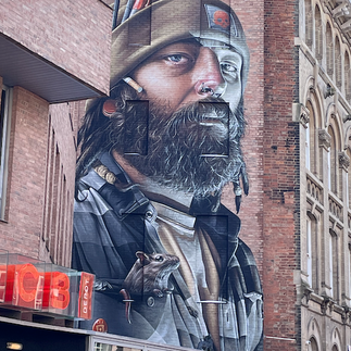 Grafitti from the Bring the Paint festival of a man wearing a hat with a mouse in his pocket, painted huge next to the LCB building on a wall