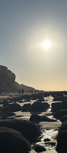rocks sun sea people in distance walking