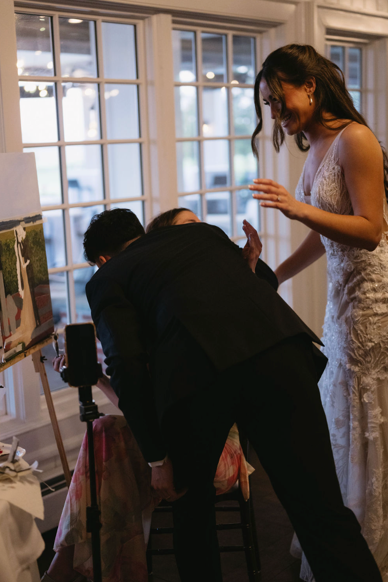 Groom hugging live wedding painter as bride reacts to live wedding painting