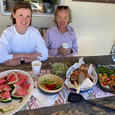 Two people enjoying a freshly prepared dinner with a variety of dishes, including watermelon, salads, and bread, at an outdoor table.