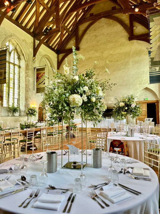 round table with flowers on a tall metal towers; inside a medieval Great Hall