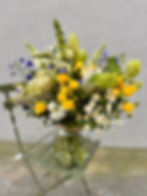 yellow, white, blue and green flowers and foliage bouquet in a glass vase on a green chair