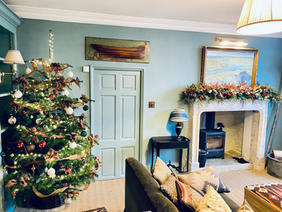 room with furniture, Christmas tree, decorated fireplace, door, table with lamp, pictures and sofa