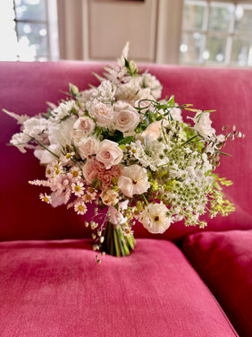 garden style bridal bouquet on a raspberry coloured sofa beside a window