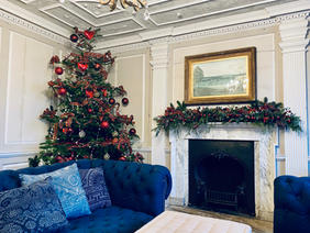 Christmas tree, fireplace with garland on the mantlepiece and a blue sofa