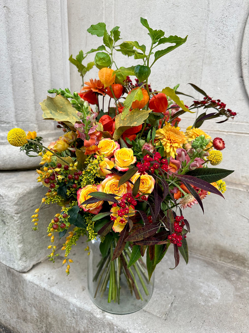 Thumbnail: Autumnal orange, yellow and red seasonal flowers with greenery arranged in a vase
