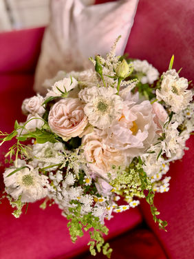 garden style bridal bouquet on a raspberry coloured sofa beside a window