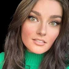 a white woman with brown hair, green eyes, and wearing a light green turtleneck