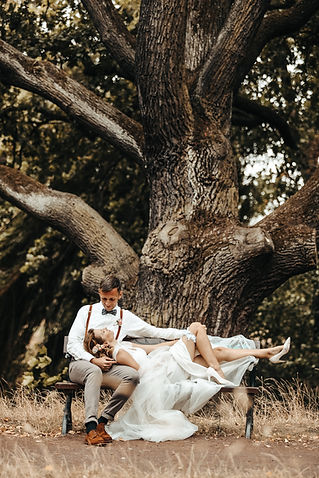 Ein Hochzeitspaar sitzt im Stadtpark Magdeburg auf einer Bank und schaut sich verliebt an.