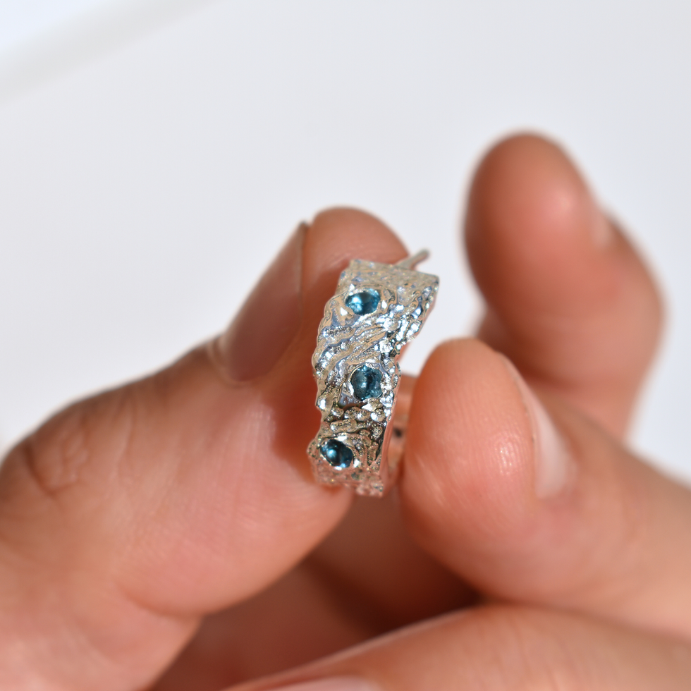Thumbnail: Close-up photo of handmade sterling silver hoop earring with London Blue Topaz gemstones, featuring a sculptural molten textu