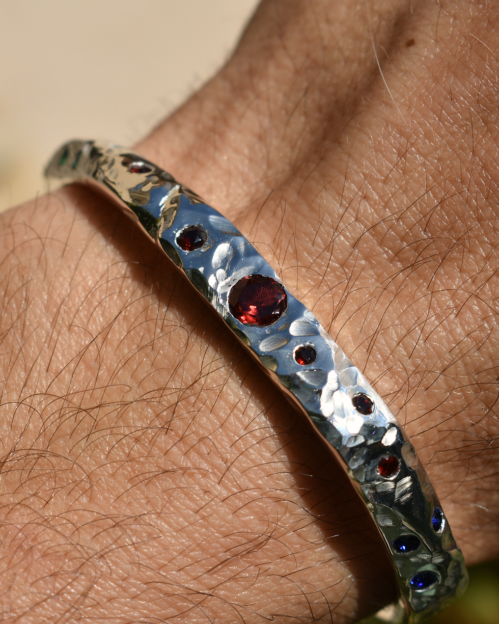 Handmade sterling silver cuff bracelet with raw texture and garnet stones, worn on wrist, organic artisan jewelry