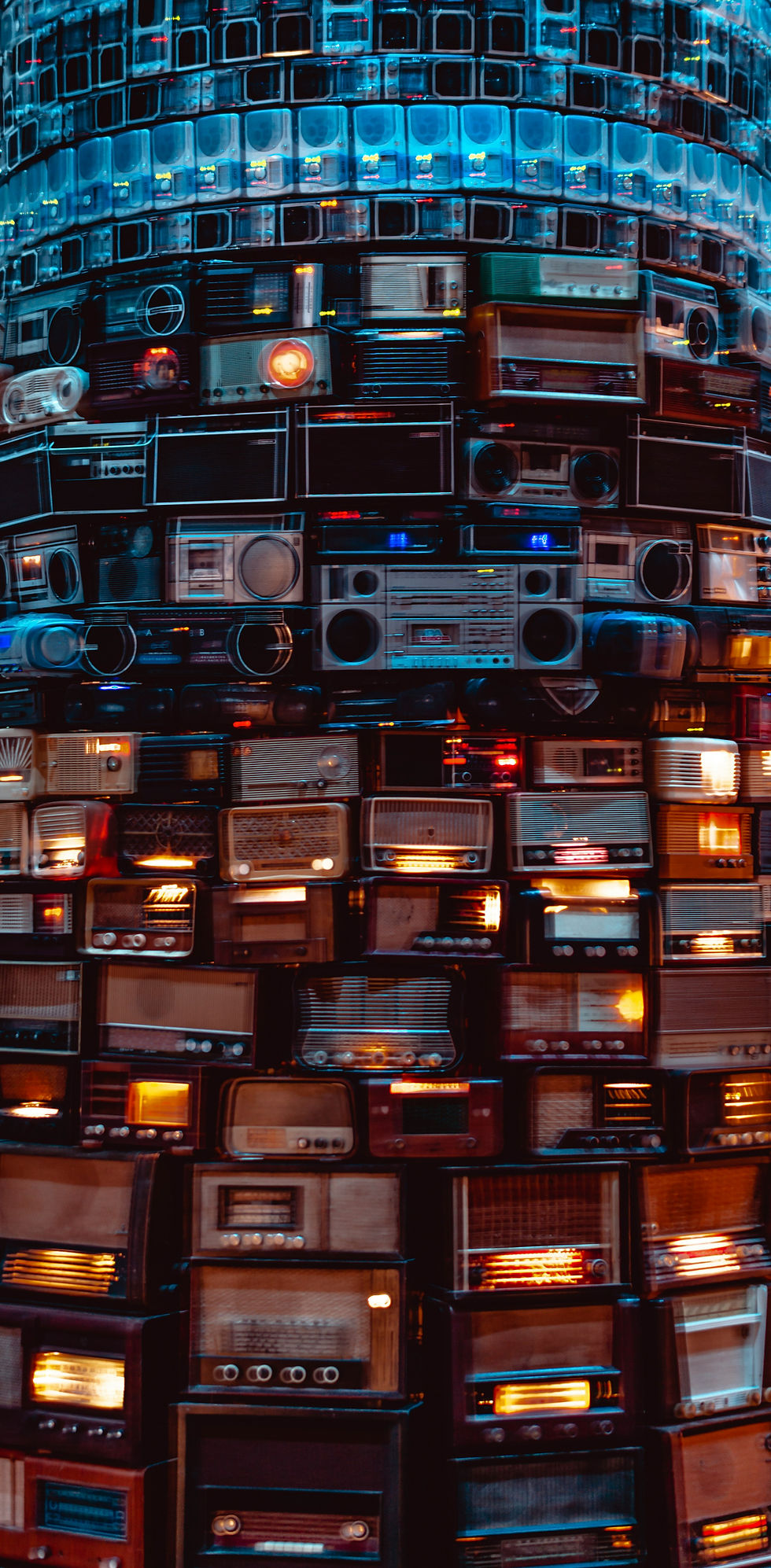 A vibrant wall of vintage radios stacked in a mosaic pattern, featuring various styles, sizes, and glowing dials, creating a retro aesthetic.
