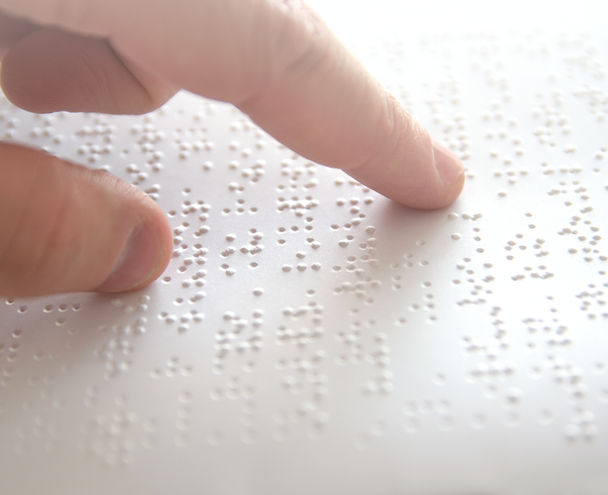 Braille paper with a persons finger running across the page.
