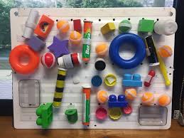 Image shows a position board with everyday items to explore including pipes, medication containers, large lego pieces, blocks, rings, baking utensils, etc.