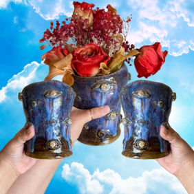 three hands holding a ceramic vase with a melted blue and brown glazed look, eyes attached, holding an assortment of red flowers on a blue cloudy sky background 