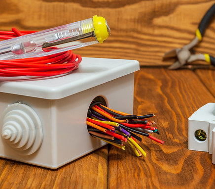 Bundle of multicolored electrical wires emerging from a plastic junction box with tester tool on wooden surface