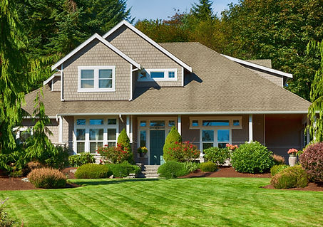 Beautifully landscaped front yard featuring a neatly trimmed green lawn, vibrant shrubs, and a modern suburban house with a grey facade and large windows