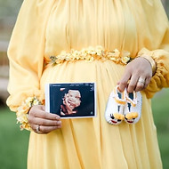 A mother in a yellow dress holding ultrasound of unborn baby