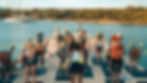 Wellness retreat participants doing resistance band exercises on yoga mats set on a dock surrounded by turquoise Greek waters.